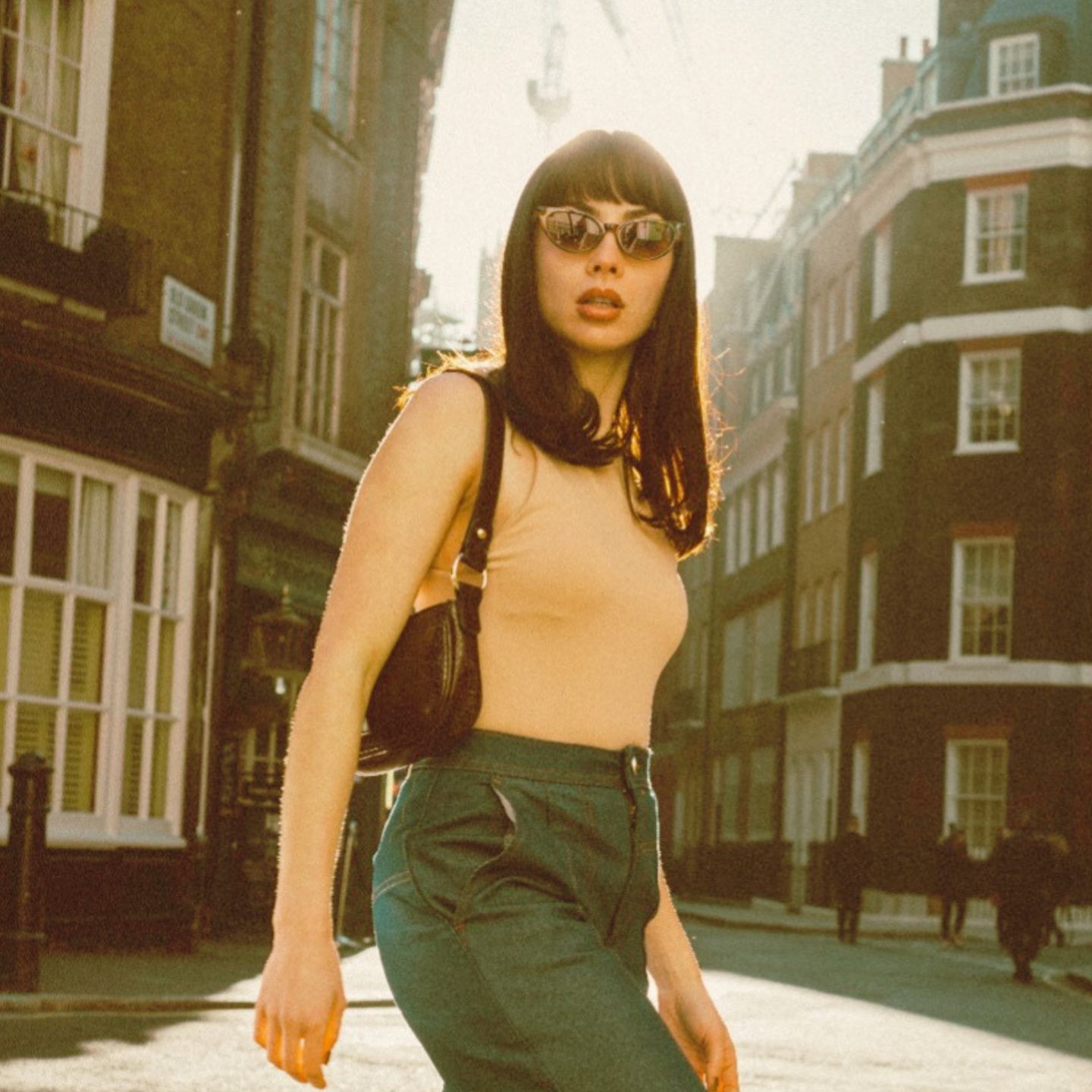 Woman in sunglasses with small purse walking on the streets of London with brick buildings behind her