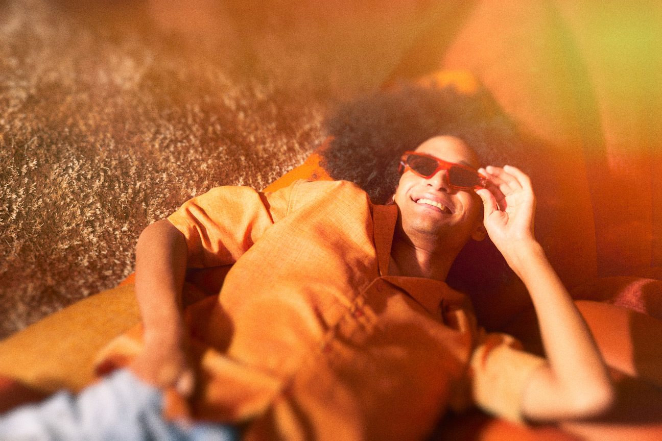 Man in orange shirt and red sunglasses smiling and laying on orange couch