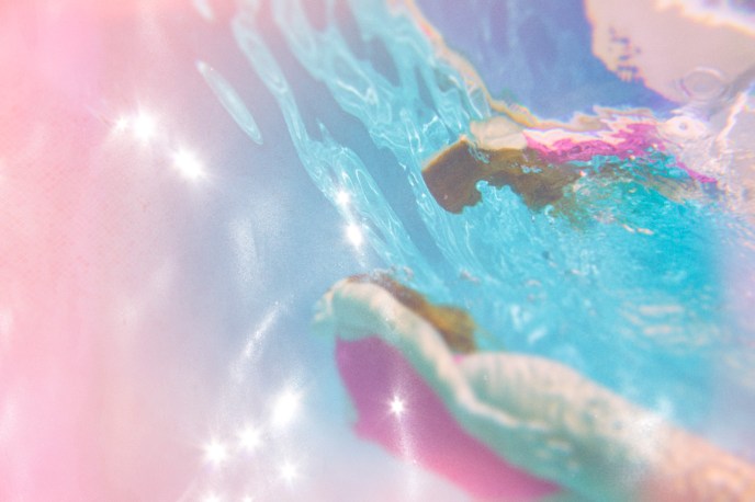 Woman in pink bathing suit swimming underwater in sparkling blue pool