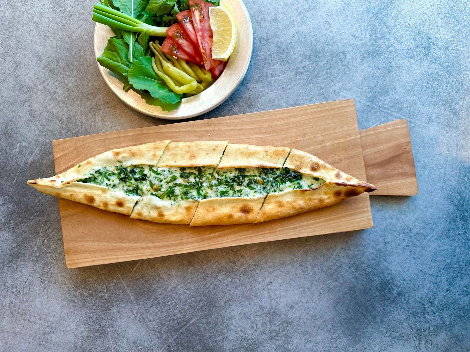 Large bread and spinach dish on a wooden board with veggies on the side