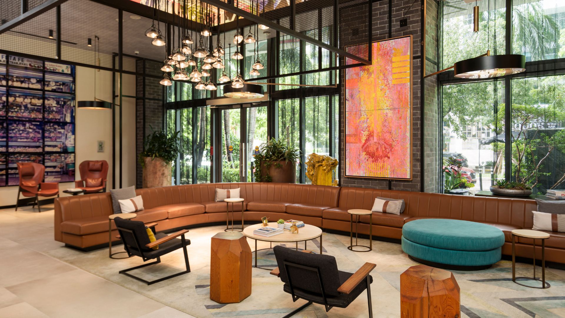 Hotel lobby with large chestnut leather sofa, teal ottoman, mixed chairs, and pendant lighting