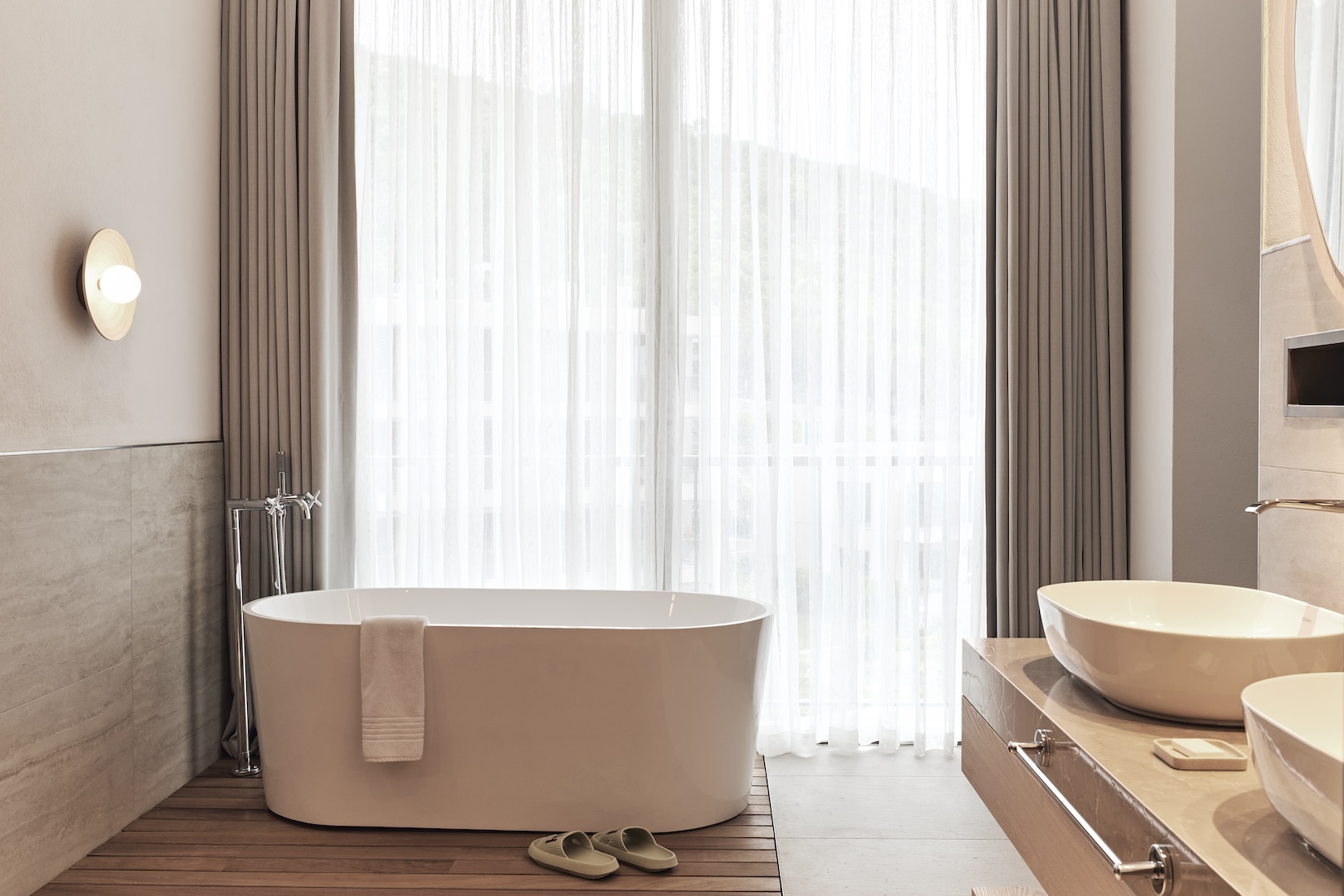 Large soaking tub in a bathroom with floor to ceiling windows covered by curtain