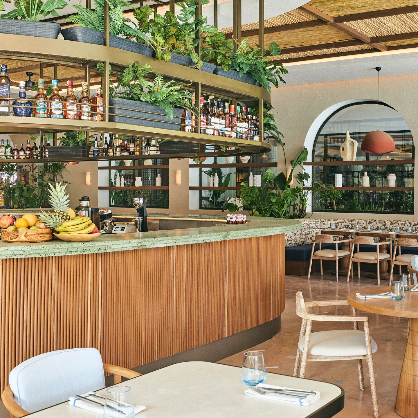 Large wooden bar with green top and plants throughout in a dining space