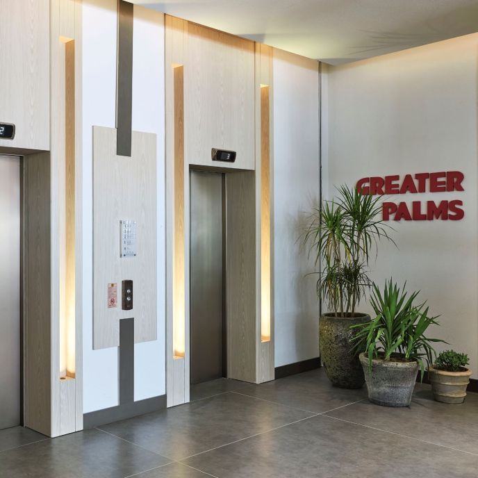 Elevator bank with sign that reads Greater Plams and plants on the ground