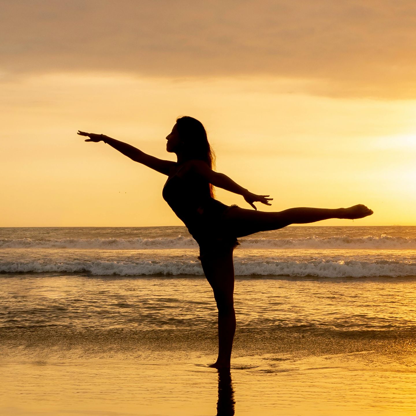 Woman doing a yoga post on a sandy beach while the sun sets