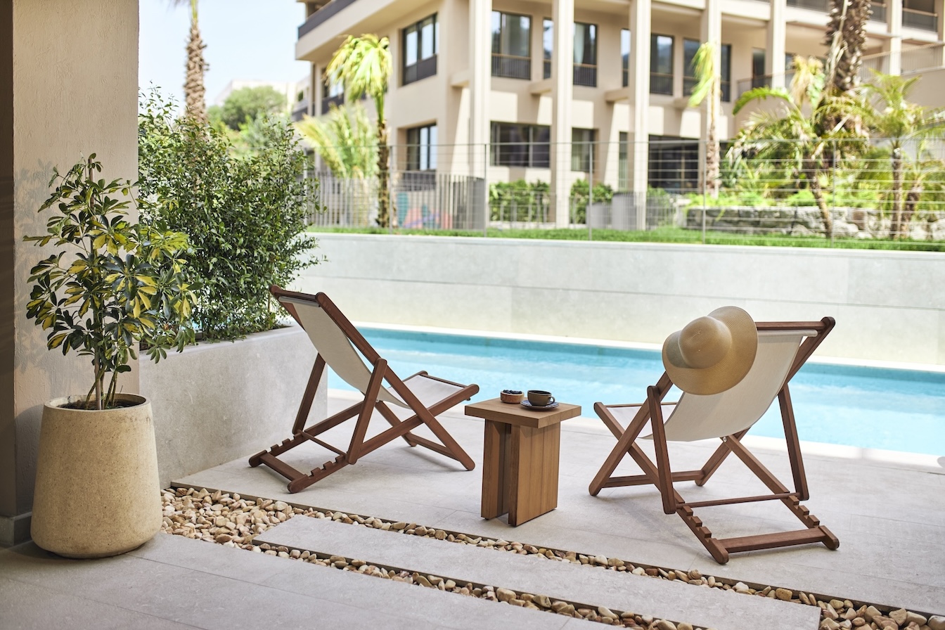 Two outdoor chairs with small table in between them face a pool