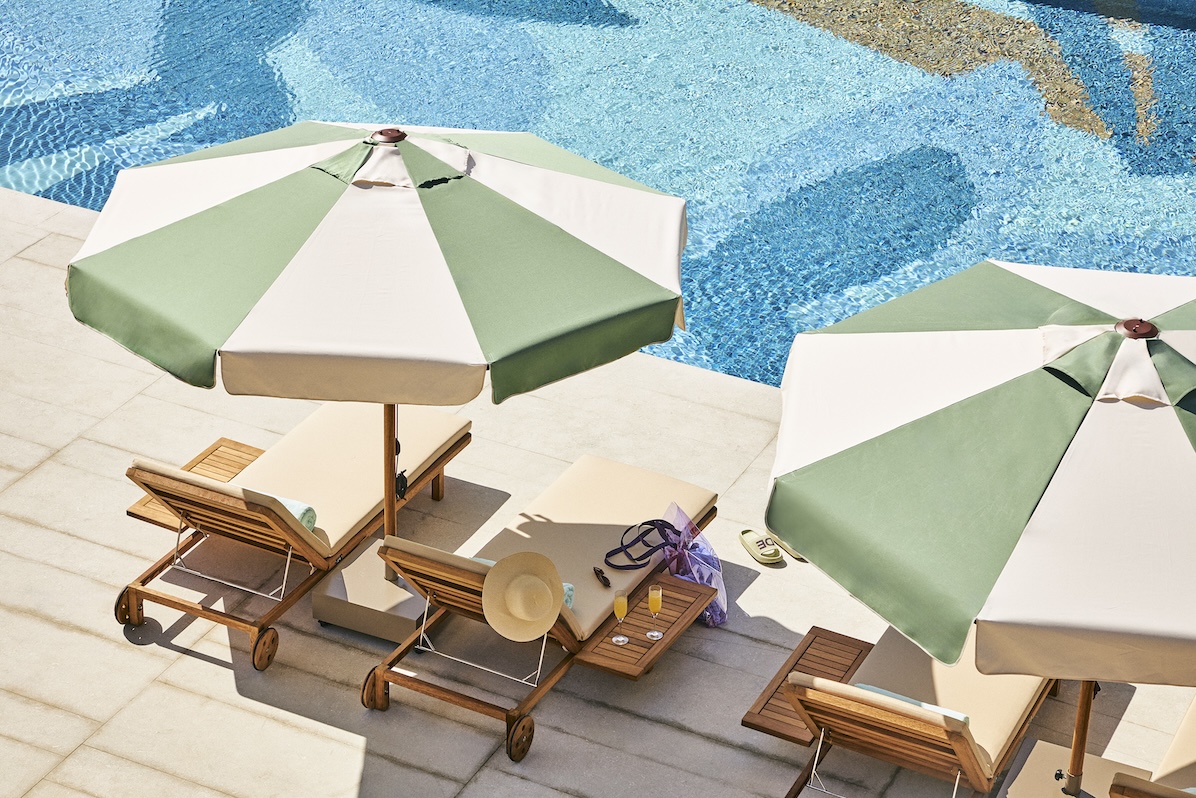 Green and white striped umbrellas over beige chaise lounges with a blue pool in the background