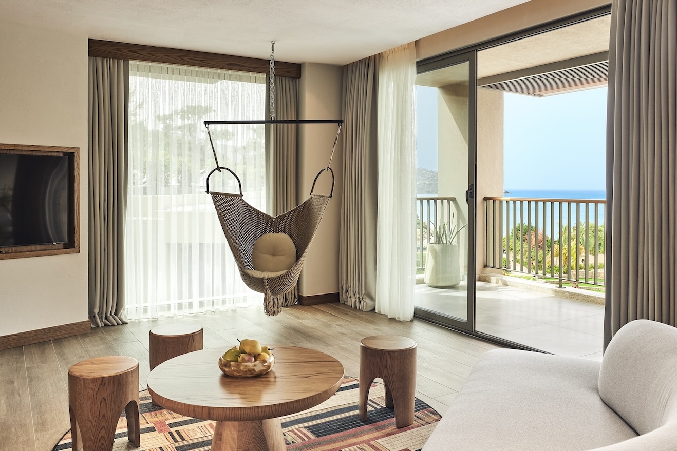 Hammock hanging in a room with small round coffee table and stools with large glass sliding doors looking out onto a balcony