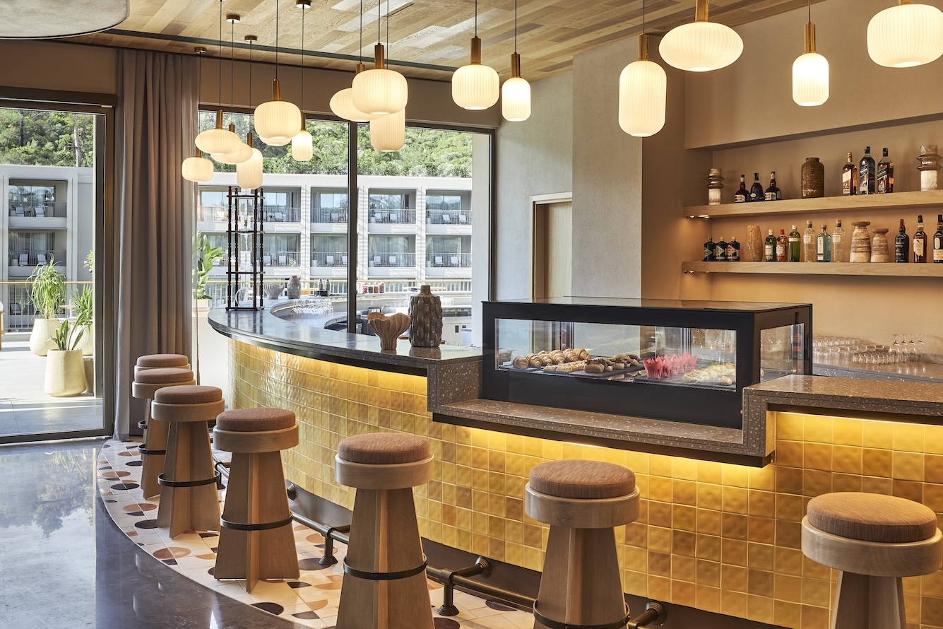 Bar with yellow tiles and modern gold bar stools and pendant lights of different shapes ahead