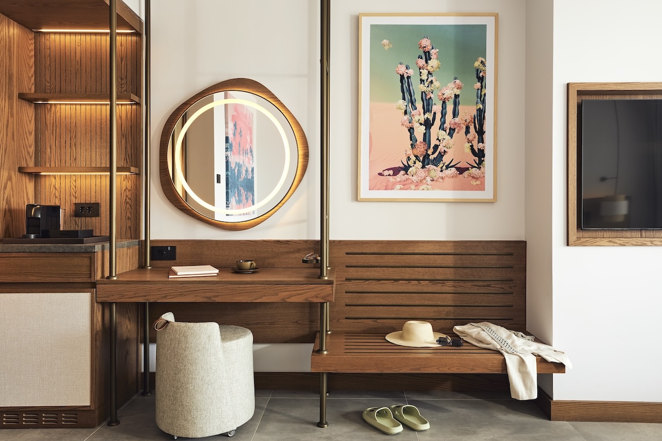 Wooden vanity with circular mirror, beige stool, and wooden bench with framed artwork above it
