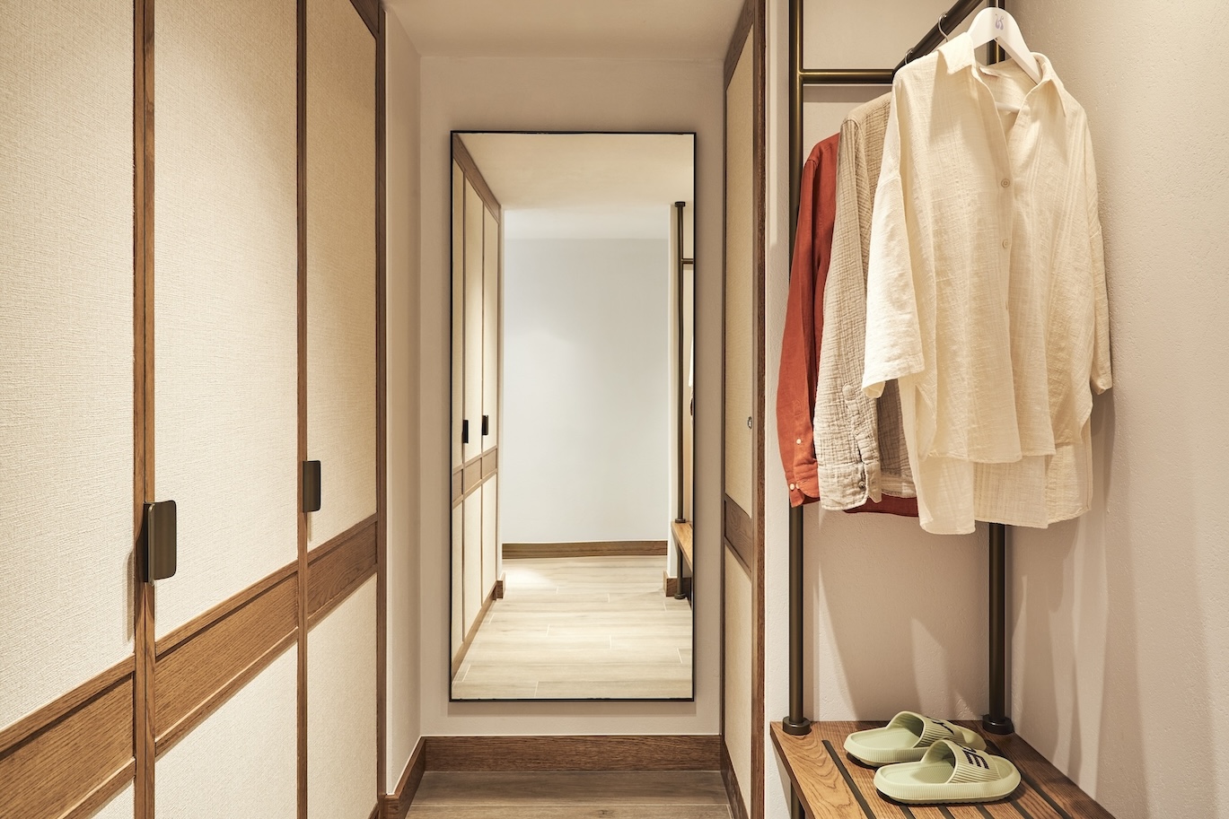Hallway view of a wardrobe with clothes hanging and a full-length mirror