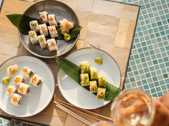 Three plates of sushi on a wooden board on top of a blue-tiled floor