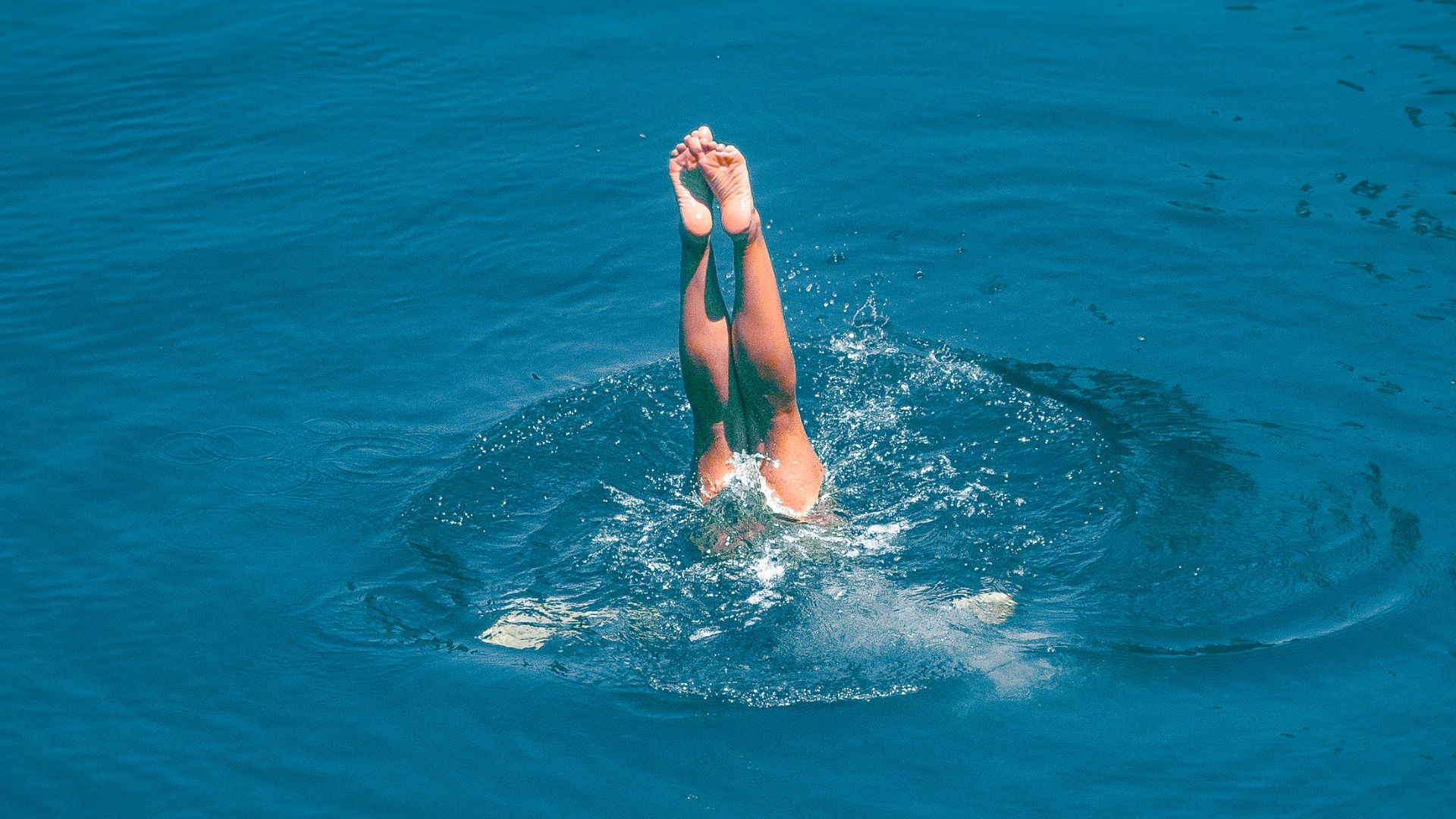 Blue water with someone's legs sticking out after diving into the water