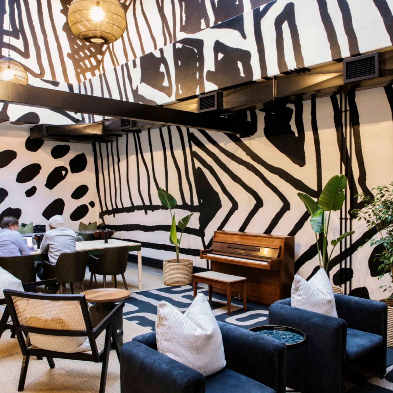 Hyde Johannesburg's workspace with black and white artwork on the walls, piano placed in the room and 2 blue velvet armchairs with a coffee table in between.