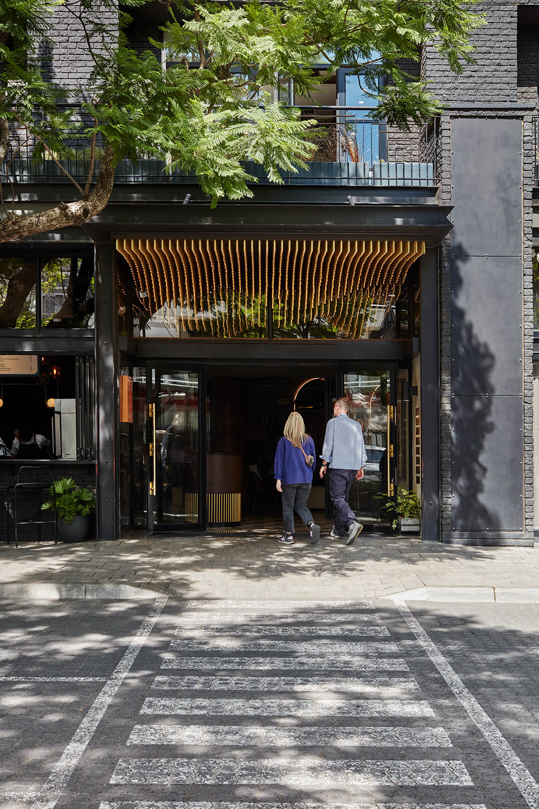 A couple walking into the hotel entrance with trees lining the street.