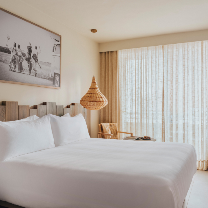 A king sized bed with artwork above and light hanging from the ceiling