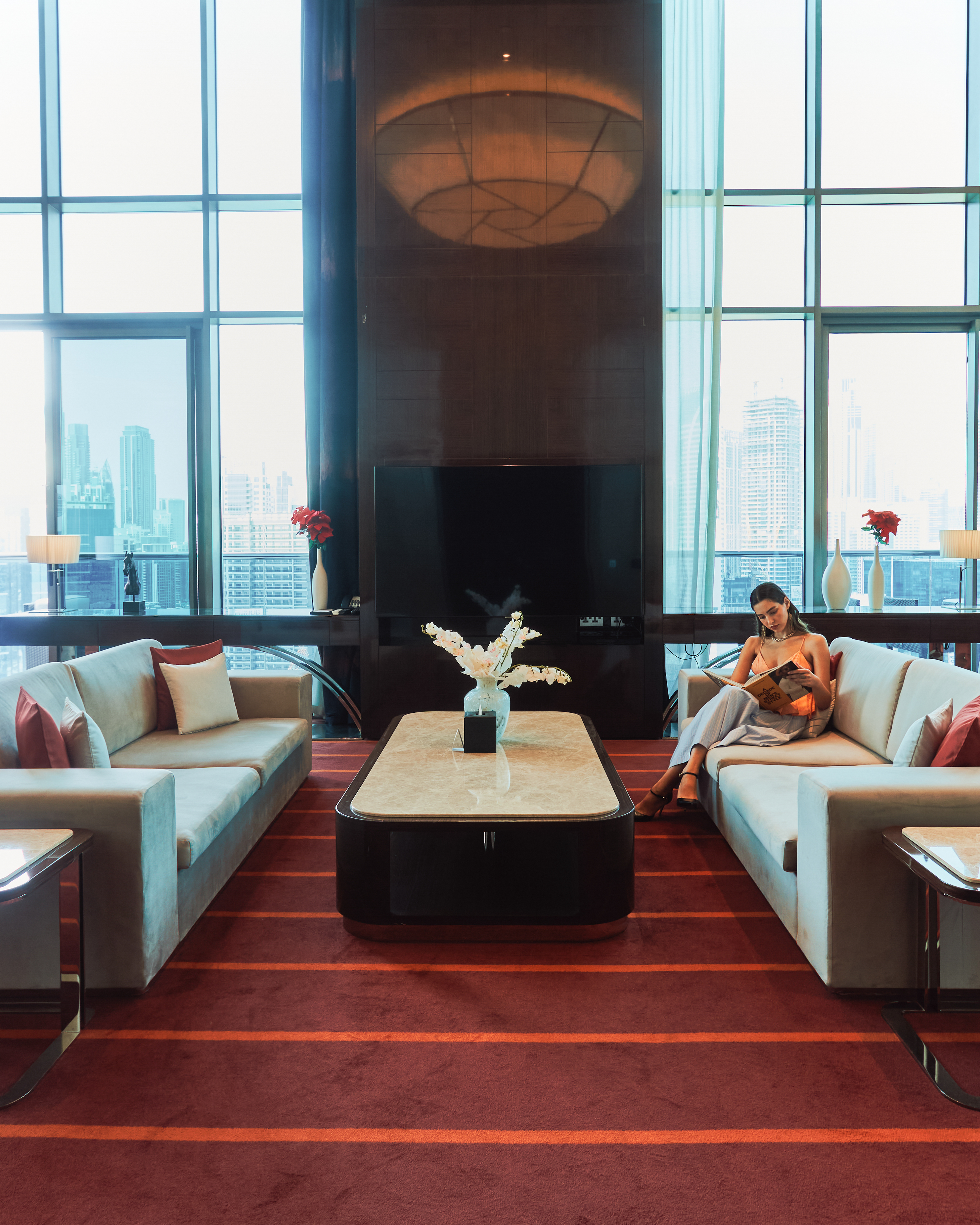 A lady sitting on a sofa in the living room of a penthouse, reading a book